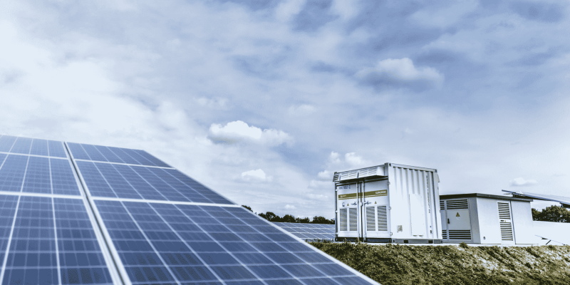 Generador y paneles solares en un campo, bajo un cielo nublado.